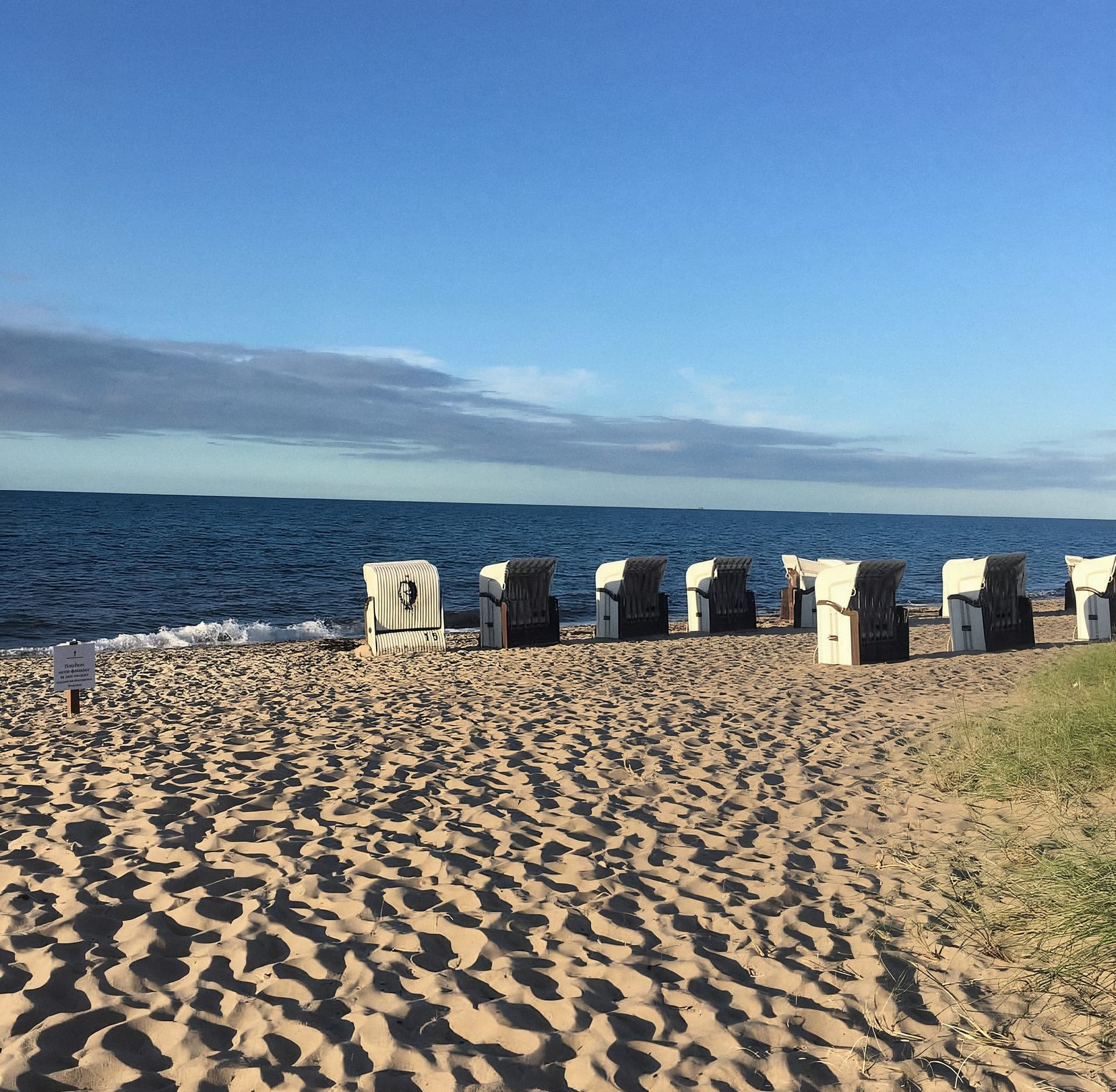En række strandkurve i sandet, bagved Østersøen under blå himmel