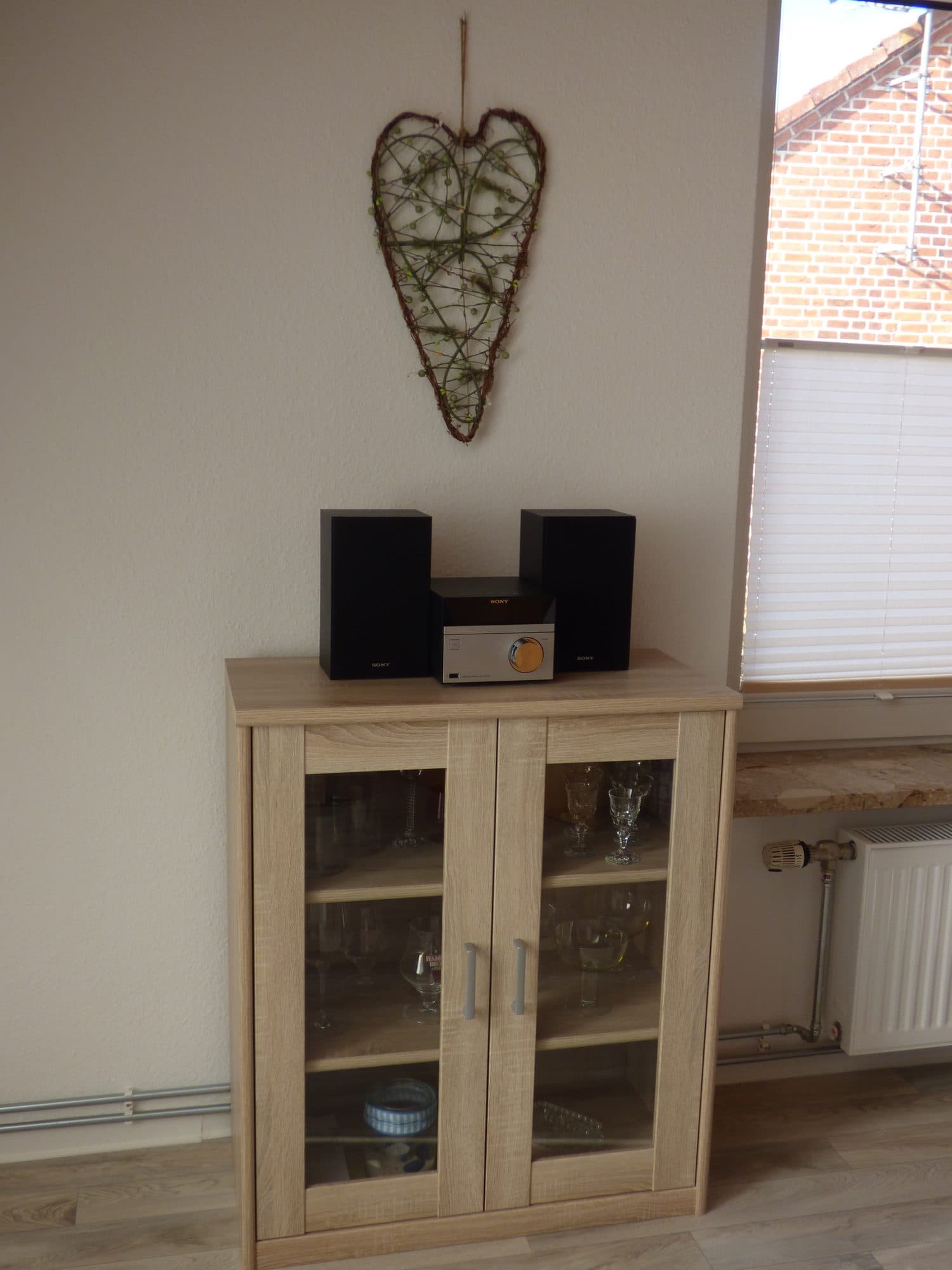 Sideboard mit Stereoanlage, darüber ein geflochtenes Herz an der Wand